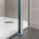 Clear forked-foot seal fitted at the base of a glass shower door, sponge and bottle behind.