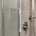 White hook seal fitted at a glass shower door edge, chrome mixer tap behind.