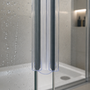 Clear seal fitted between two glass shower panels, bathroom niche with plant and bottles behind.