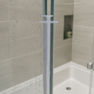 Clear bi-fold seal fitted to a wet glass shower panel edge, bathroom shelf and soap bottle behind.