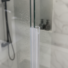 Clear seal down a wet glass screen edge, black shower valve and hose reflected in marble tiles behind