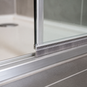 Grey brush seal under the bottom rail of a sliding shower door, bristles meeting an aluminium track