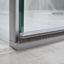 Brush seal along the base of a glass shower enclosure, bristles brushing a chrome frame section