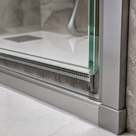 Brush seal on the bottom rail of a glass shower door beside a chrome corner post