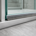 Grey brush seal along the bottom of a glass shower door, bristles brushing an aluminium threshold