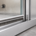 Brush seal below a wet glass shower door, bristles sweeping the chrome frame rail