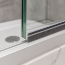 Brush seal on the frame rail beneath a glass shower panel, bristles touching a white tray