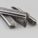 Brush seal offcuts crossed on a grey surface, clear ribbed carrier visible on the top piece
