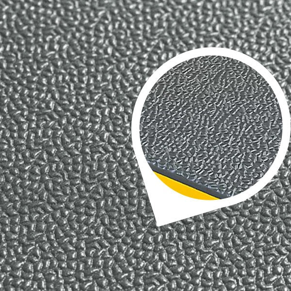 Close-up macro image of the heavy-duty, dark grey, pebbled surface of an anti-fatigue mat. The textured PVC foam is wear-resistant and non-slip, providing cushioned support for workstations, garages, and industrial use. An inset magnifies the texture and shows the mat's thickness with a yellow layer on the bottom.