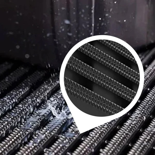 Close-up of a black, heavy-duty industrial matting roll with water splashing across the surface, demonstrating its suitability for wet areas. The mat's surface features deep, continuous ribs. An inset circle magnifies the non-slip, high-traction, diamond pattern on the ribs, highlighting the UV-resistant floor mat's superior grip for industrial and outdoor use.
