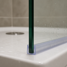 Close-up of the clear seal on the glass edge at a shower tray corner, drain visible behind
