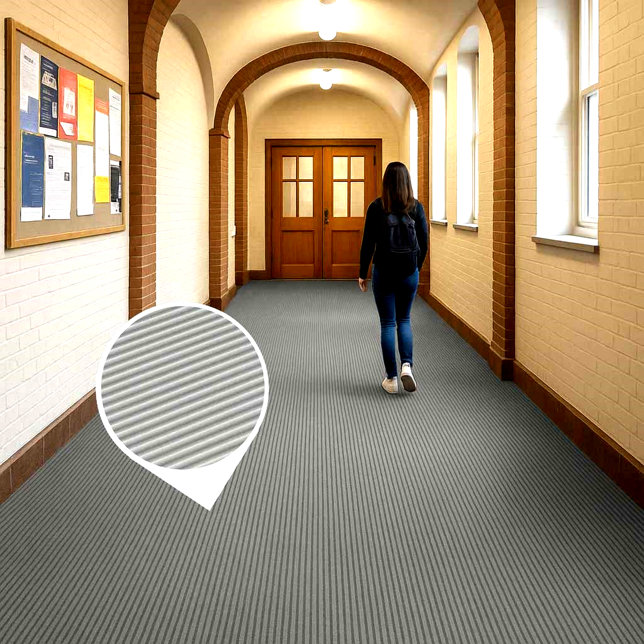 Grey fine ribbed PVC matting roll covering the floor of a long, arched school or university hallway. A student walks on the slip-resistant matting, demonstrating its use as a long runner that is chemical and oil resistant for high-traffic public or institutional areas.