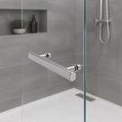 Chrome bar handle fitted to a glass shower panel, grey tiled niche with a plant and shower valve behind