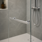 Chrome bar handle on a glass shower screen, grey marble-effect tiles and a riser rail behind