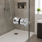 Chrome shower door knob with black seal ring on a glass panel, walk-in shower and white tray behind