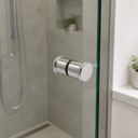 Chrome knob fitted near the edge of a glass shower screen, grey tiles and potted plants behind