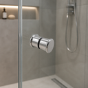 Chrome shower door knob on a glass panel, grey tiled walk-in shower with hose and linear drain behind