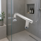 Chrome offset shower door handle on a glass screen, grey concrete-effect tiles and shower riser behind