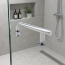 Chrome offset handle on a glass shower screen, grey tiled alcove with toiletries and a plant behind