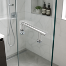 Chrome offset shower door handle on a glass door, white patterned tiles and shower hose behind