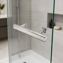 Chrome T-bar handle fitted to a glass shower door, light grey tiles, niche and vanity unit behind