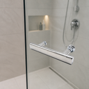 Chrome T-bar handle on a glass shower door, cream tiles with a lit niche and shower hose behind