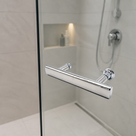 Chrome T-bar handle on a glass shower door, cream tiles with a lit niche and shower hose behind