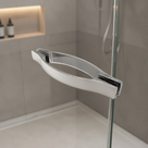 Sculpted chrome shower door handle on glass, lit niche and grey tiled wall in the background