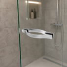 Curved leaf-shaped chrome handle on a glass shower screen, grey tiles and a mirrored niche behind