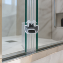 Clear M-shaped seal fitted at glass shower corner, chrome hose and plant behind