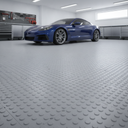 Grey studded interlocking floor tiles across a home garage, blue sports car and tool cabinets behind