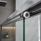 White nylon wheel seated in the chrome top rail of a sliding glass shower door, tiled shower behind
