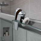 Chrome roller gripping the top edge of a glass shower door, white wheel on the rail, tiled shower behind