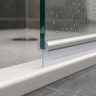 Brushed chrome seal along the base of a wet glass panel, blue-outlined blade, stone floor and drain behind