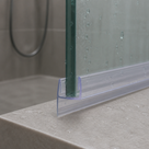 Clear J-hook seal fitted to a glass edge on a tiled bath surround, shower hose behind