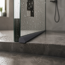 Dark grey threshold seal fitted along a wet room floor at the base of a glass shower door