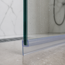 Close-up of the seal on a glass edge, floor drain and tiled wall visible behind