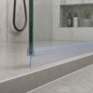 Clear tapered seal at the foot of a wet glass shower panel on a grey tiled step, shower hose behind
