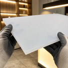 Gloved hands holding a translucent opal acrylic panel in a shop with warm backlit shelving behind