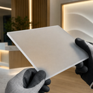 Gloved hands holding a matt frosted white acrylic panel in a softly lit reception area