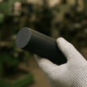 Gloved hand gripping a slim black nylon rod angled toward the viewer, green machine tools blurred behind