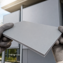 Gloved hands holding a light grey PVC sheet outside a modern clad building