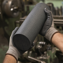 Cream-gloved hands holding a coarse-textured grey nylon billet, green machinery behind