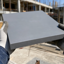 Gloved hands holding a thick mid-grey PVC panel on a building site, scaffolding behind