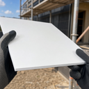 Gloved hands holding a white PVC panel in front of a scaffolded building, blue sky above