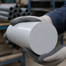 Pale grey uPVC billet cupped in grey knitted gloves, circular sawn face forward, dark pipe on racking behind