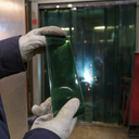 Gloved hands holding a green welding-grade PVC strip in front of a green screen curtain with an arc flashing behind