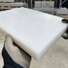 Gloved hands holding a thick milky white polypropylene slab in a yard, racked stock behind