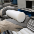 Glossy white polypropylene rod cradled in grey and cream gloves above racked white bar