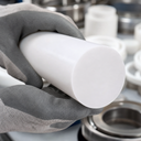 Grey glove holding a white PTFE rod, white bushes and steel bearings behind
